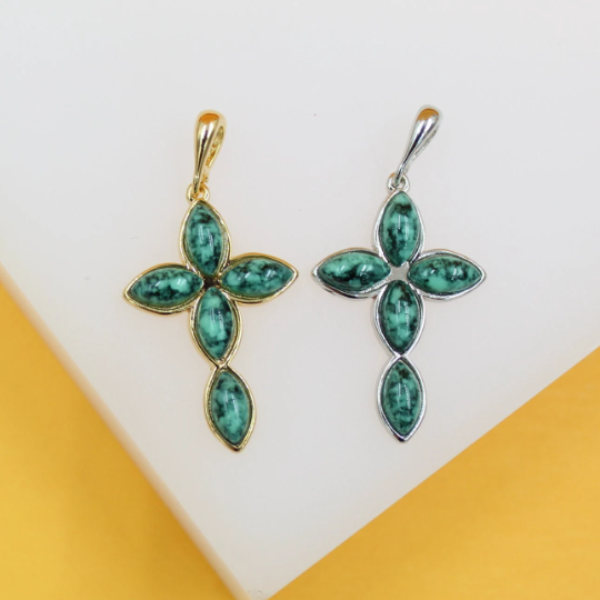Two cross-shaped pendants featuring turquoise gemstone cabochons rest on a white surface, with one set in gold and the other in silver.