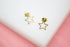 A pair of delicate gold star-shaped stud earrings rests against a white and pink background.