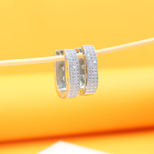 Two sparkling diamond pave huggie earrings hang delicately from a thin stick against a warm yellow background.