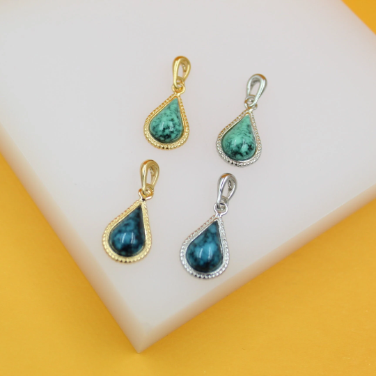 Four teardrop-shaped turquoise gemstone pendants in gold and silver settings rest on a white display surface.