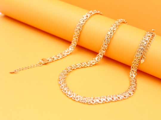 A delicate gold Byzantine chain necklace rests gracefully against a vibrant orange and yellow backdrop.