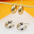 Two pairs of chunky small hoop earrings, one in gold and one in silver, rest on a white surface against an orange background.