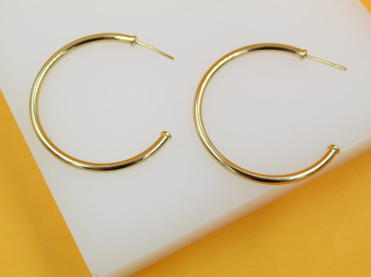 A pair of polished gold hoop earrings rests neatly on a white display surface against a vibrant orange backdrop.