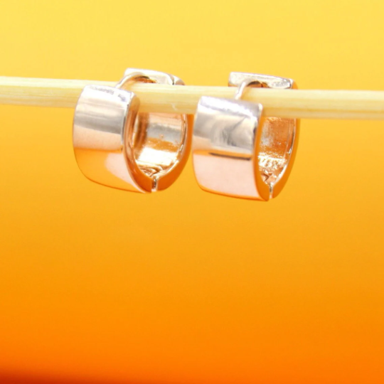 A pair of polished silver hoop earrings hangs delicately on a wooden stick against a warm yellow background.