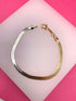 A two-tone herringbone chain bracelet made of alternating gold and silver links rests on a white display surface against a vibrant pink background.