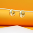 Two engraved gold hoop earrings hang delicately from a thin stick against a warm orange backdrop.