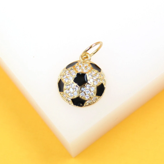 A gold soccer ball charm encrusted with sparkling cubic zirconia and black enamel rests on a white display block.