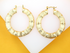 A pair of textured gold bamboo hoop earrings rests against a white and yellow surface.