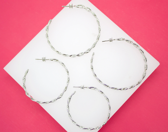 Four textured silver hoop earrings lie arranged on a white square display set against a vibrant pink background.