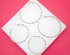 Four textured silver hoop earrings lie arranged on a white square display set against a vibrant pink background.