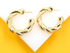 A pair of shiny gold twisted hoop earrings rest on a white surface against a bright yellow background.