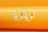 A pair of gold huggie hoop earrings embedded with sparkling cubic zirconia stones hangs delicately from a wooden stick against a bright orange backdrop.
