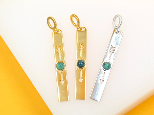 Three rectangular metal pendant charms, two in gold finish and one in silver, display cut-out arrow motifs accented with round turquoise stones.