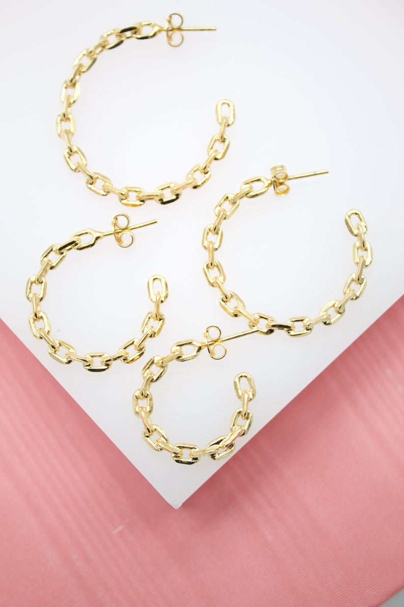 Four gold chain-link hoop earrings rest on a white and pink display surface.