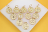 A collection of gold zodiac sign pendants with sparkling crystal accents rests on a white display block against a yellow background.