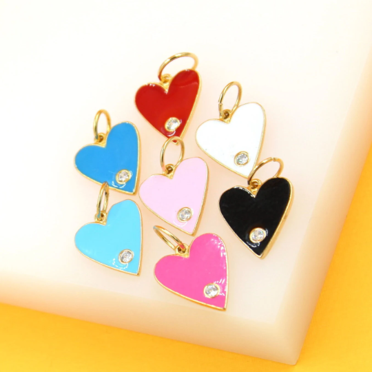A colorful collection of gold-rimmed heart charms with sparkling cubic zirconia stones rests on a soft surface.