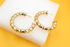 Two chunky gold hoop earrings with a textured spiral design rest on a white display stand against a vibrant yellow background.