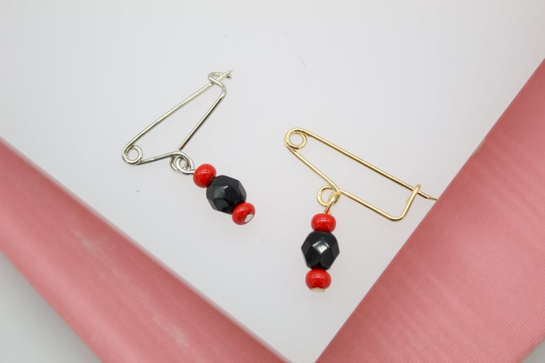 Two handmade safety pin earrings featuring vibrant red and faceted black beads dangle against a white background.