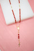 A delicate gold rosary necklace features vibrant red crystal beads and a matching crucifix.
