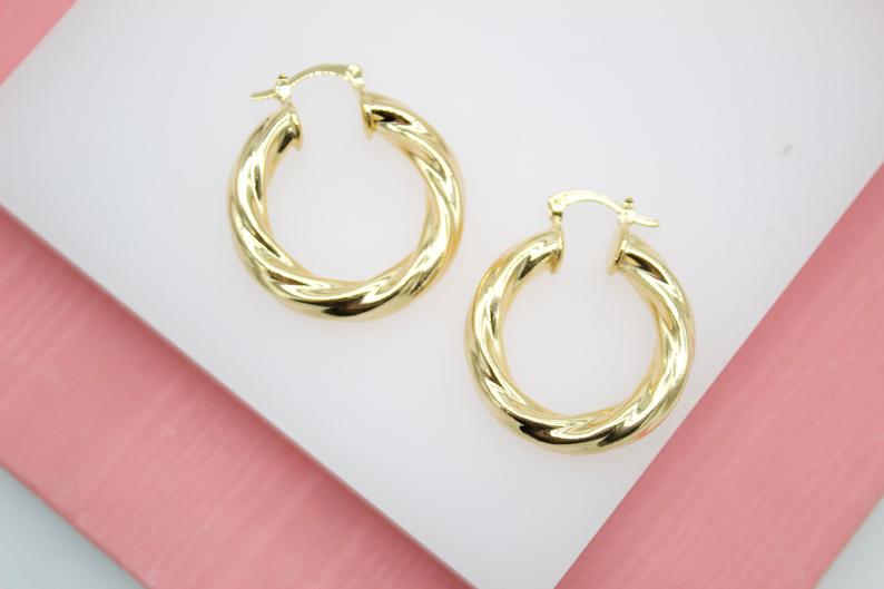 A pair of polished gold twist hoop earrings rest on a white and pink surface.