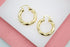 A pair of polished gold twist hoop earrings rest on a white and pink surface.