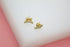 A pair of gold curved stud earrings adorned with sparkling cubic zirconia stones rests on a white surface against a soft pink background.