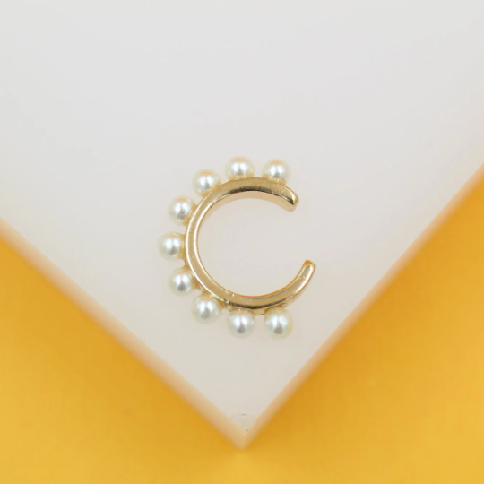 A gold ear cuff adorned with small white pearls rests against a minimalist white and yellow display.