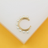 A gold ear cuff adorned with small white pearls rests against a minimalist white and yellow display.