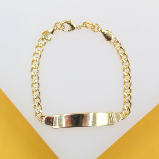 A shiny gold curb chain ID bracelet rests on a white and yellow surface.