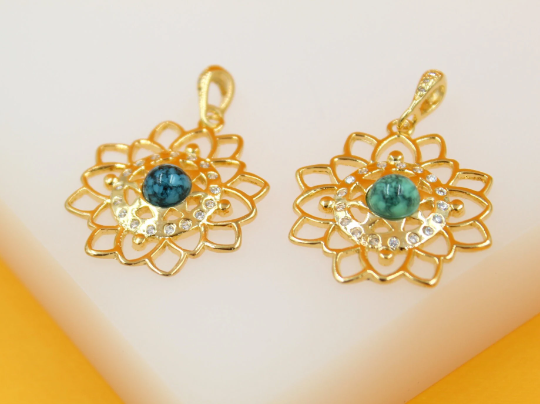 Two gold lotus flower pendants featuring central turquoise stones and sparkling cubic zirconia accents rest side by side on a light surface.