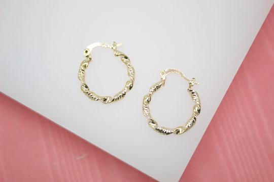 A pair of twisted gold hoop earrings rests against a white and pink background.