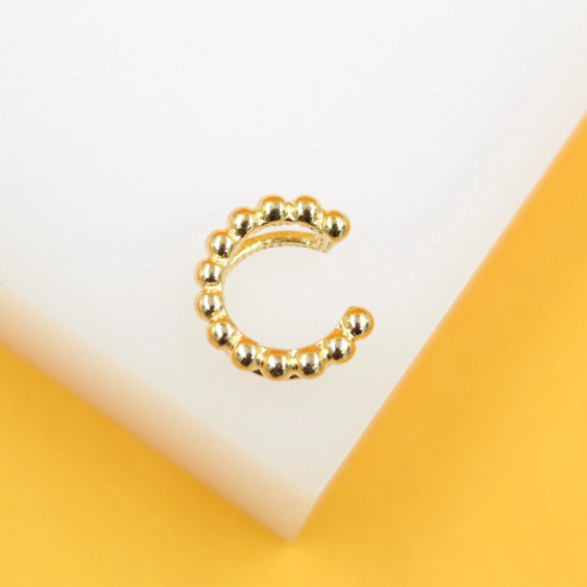 A shiny gold beaded ear cuff rests on a white and yellow display surface.