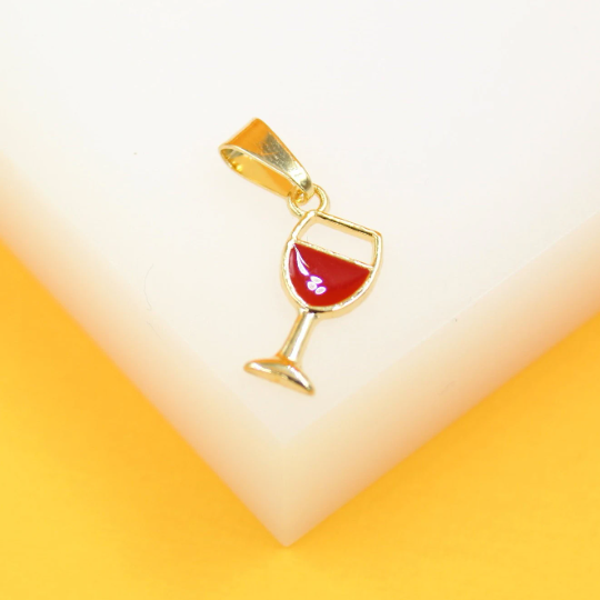 A gold wine glass pendant featuring red enamel rests on a white and yellow surface.