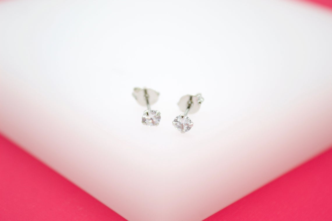 A pair of sparkling solitaire stud earrings rest elegantly on a white display stand.