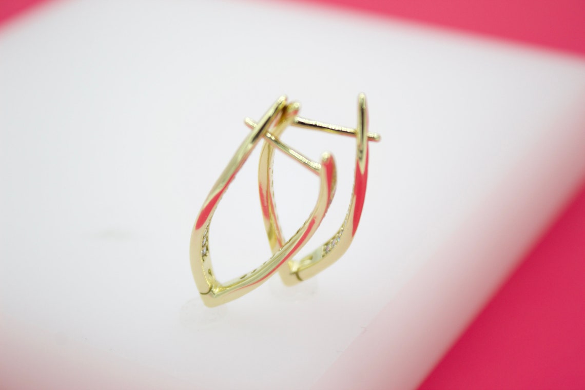 A pair of elegant gold hoop earrings rest on a white surface against a pink background.