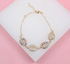 A delicate gold chain bracelet features four glittering shell charms accented with colorful zirconia stones, resting against a white and pink background.