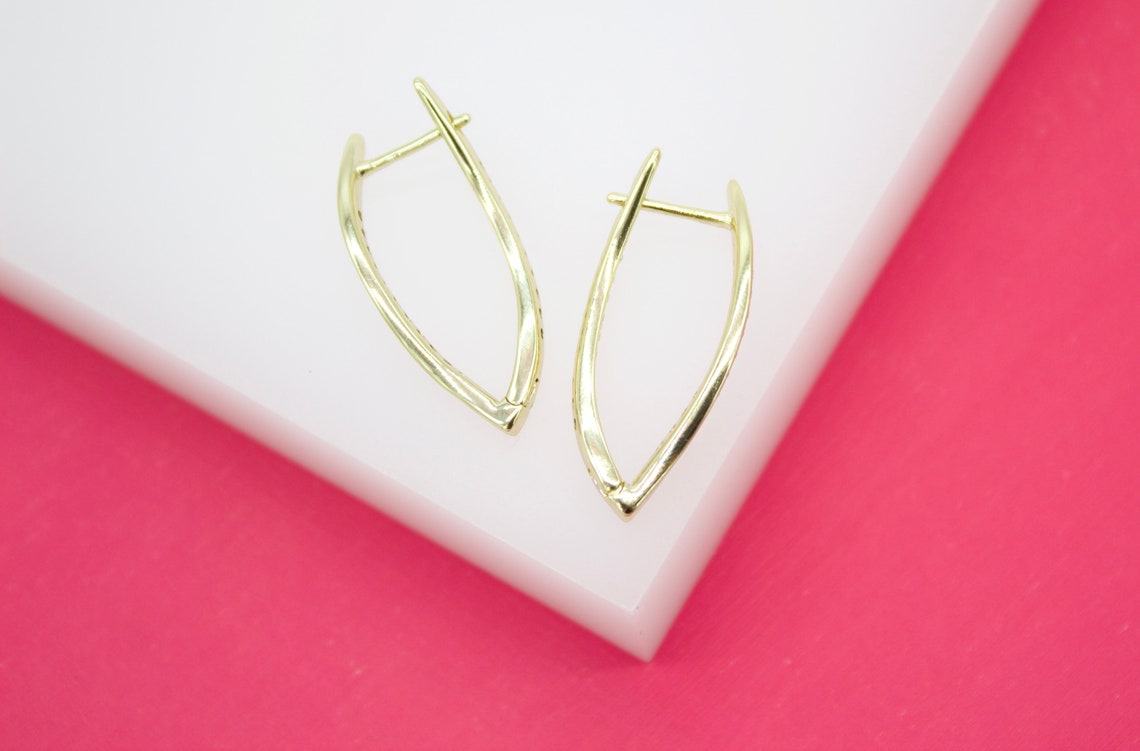 A pair of elegant gold hoop earrings rests on a white display against a vibrant pink background.