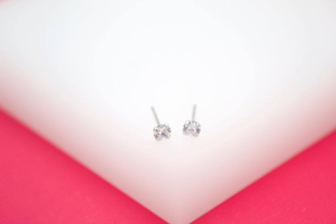A pair of sparkly silver stud earrings rests on a bright white and pink display.