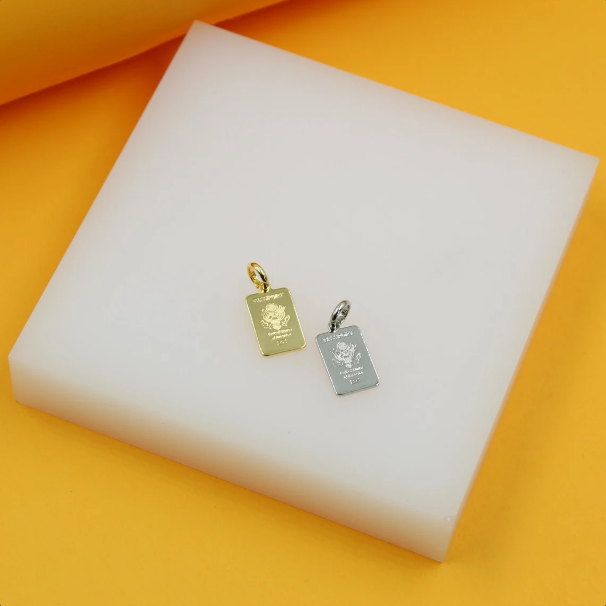 A gold and a silver passport-shaped pendant rest side by side on a white display block.