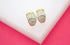 A pair of gold huggie hoop earrings featuring pavé-set clear cubic zirconia stones rests on a white display against a vibrant pink background.