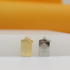Two passport-shaped charms, one gold and one silver, sit upright against a clean white and yellow background.