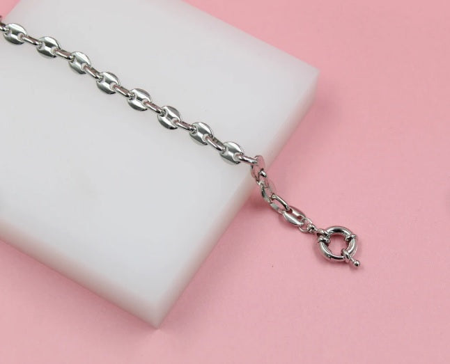 A shiny silver chain bracelet rests on a white display block against a soft pink background.