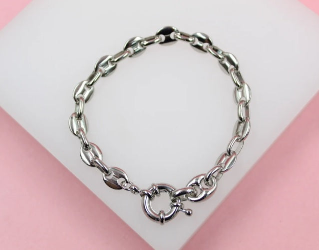 A polished silver chain bracelet rests neatly on a white display surface against a pink background.