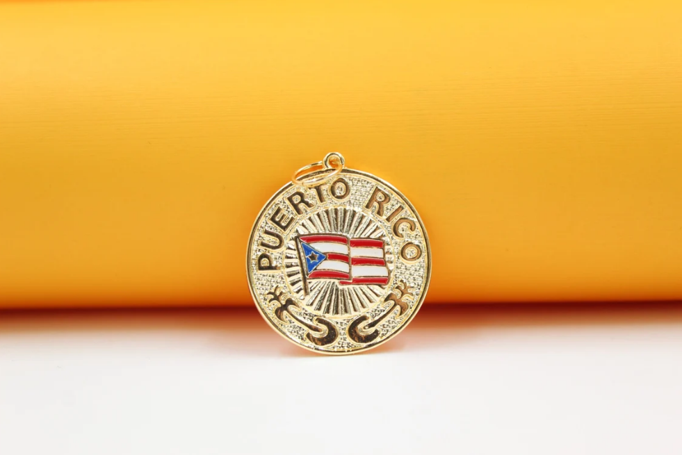 A gold Puerto Rico pendant featuring an enameled flag rests against a warm yellow and white background.