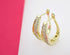 A pair of elegant gold huggie earrings encrusted with sparkling cubic zirconia stones rests against a pink and white background.