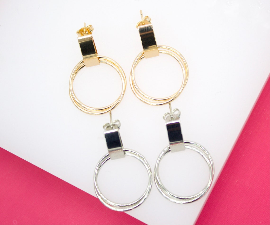 Two-toned drop earrings feature a combination of gold and silver interlocking hoop designs resting on a white display surface.