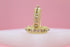 A pair of intricate gold hoop earrings embellished with small sparkling diamonds rest on a white surface against a soft pink background.