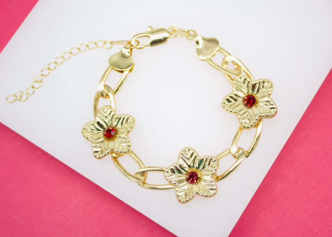 A gold link chain bracelet features three flower-shaped charms adorned with sparkling red crystal centers.