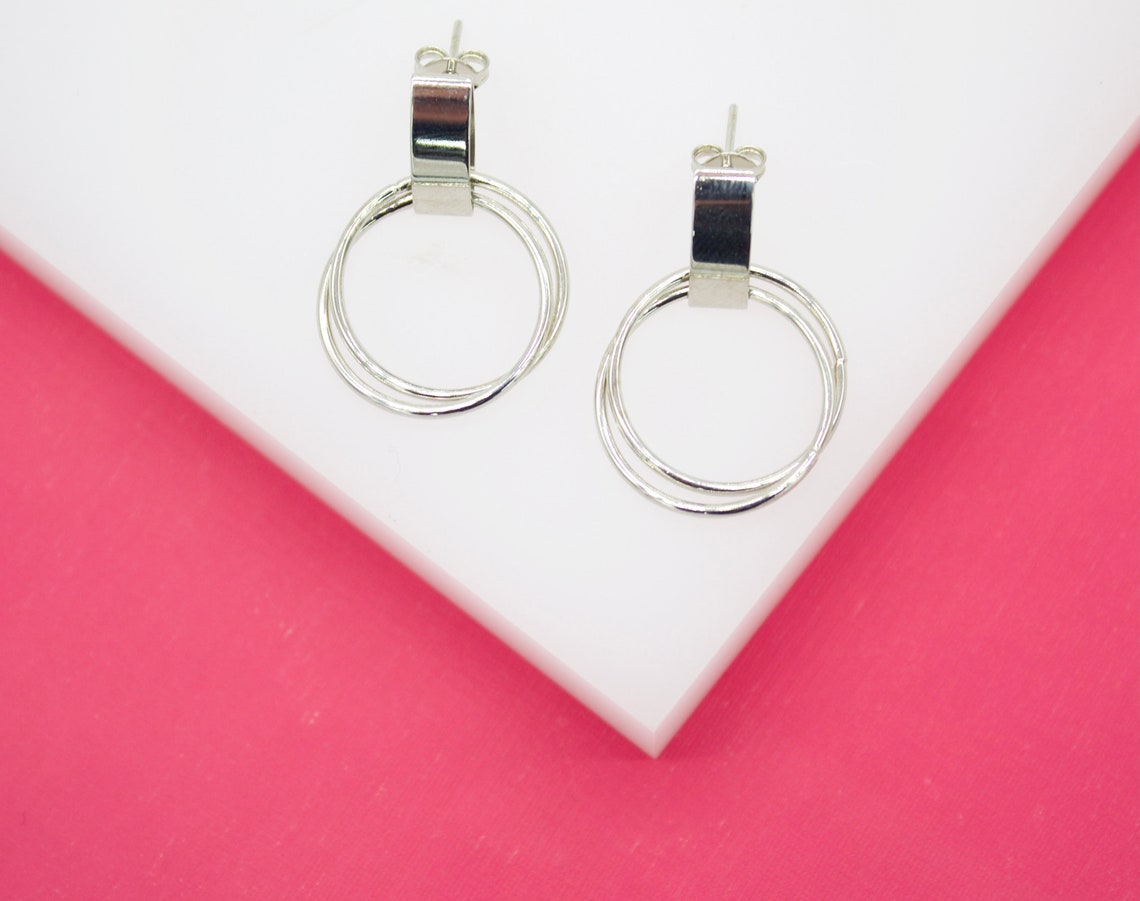 A pair of silver hoop earrings rests on a white display surface against a vibrant pink background.