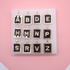 A white display board showcases twelve rectangular gold initial alphabet pendants featuring sparkly rhinestone letters set against a black background.